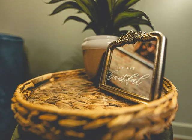A gold mirror and plant on a woven side table