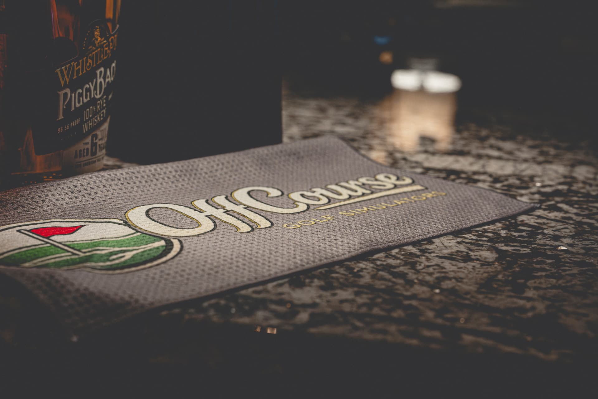 Off Course branded bar mat with whiskey bottle on a granite counter